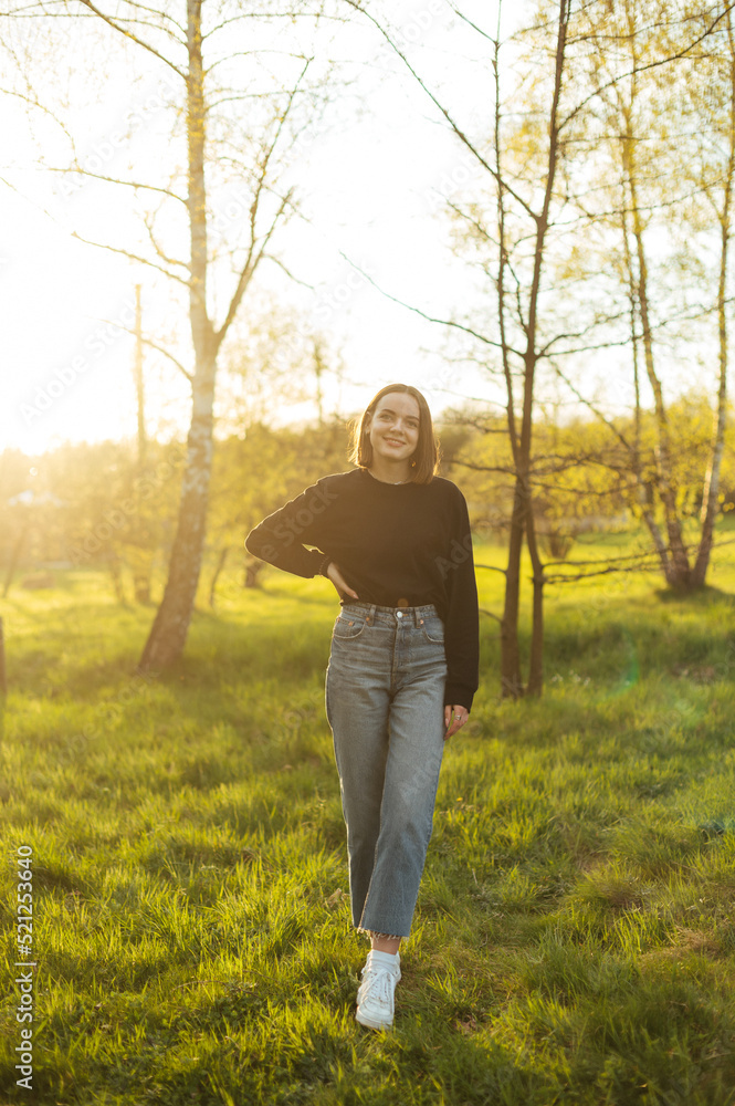 Full length portrait of an attractive woman in casual clothes standing outdoors in the park and looking at the camera with a smile on her face. Full length portrait of an attractive woman in casual clothes standing outdoors in the park and looking at the camera with a smile on her face.
