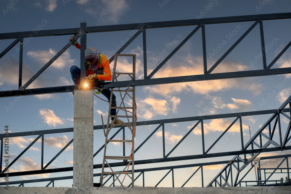 Welders wear safety belts and plastic helmets to weld steel structures.