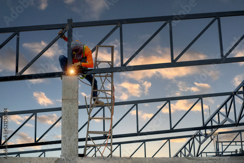 Welders wear safety belts and plastic helmets to weld steel structures.