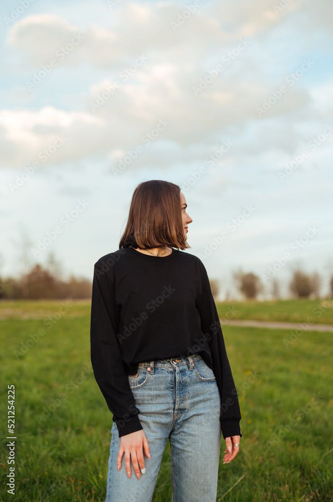 Portrait of an attractive woman in stylish casual clothes in a field in nature, posing for the camera, looking away