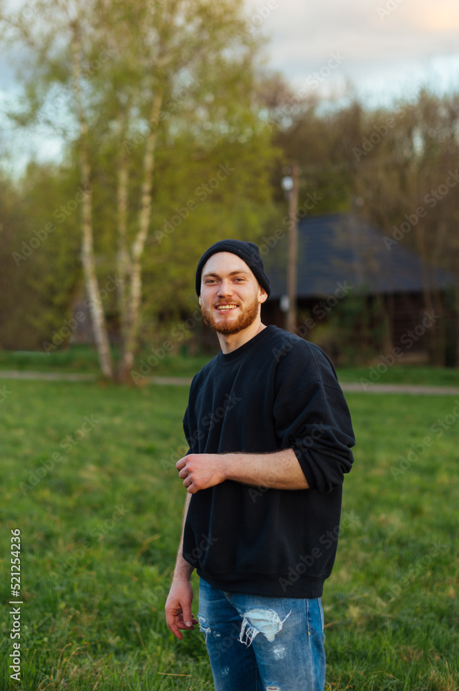 Portrait of a stylish young man in a cap standing outdoors in the park and looking at the camera with a smile on his face. Portrait of a stylish young man in a cap standing outdoors in the park and looking at the camera with a smile on his face.