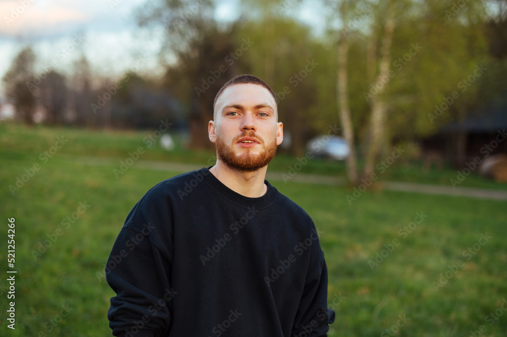 Handsome young man with a beard is standing in the park outdoors at sunset and looking at the camera with a smile on his face. Handsome young man with a beard is standing in the park outdoors at sunset and looking at the camera with a smile on his face.