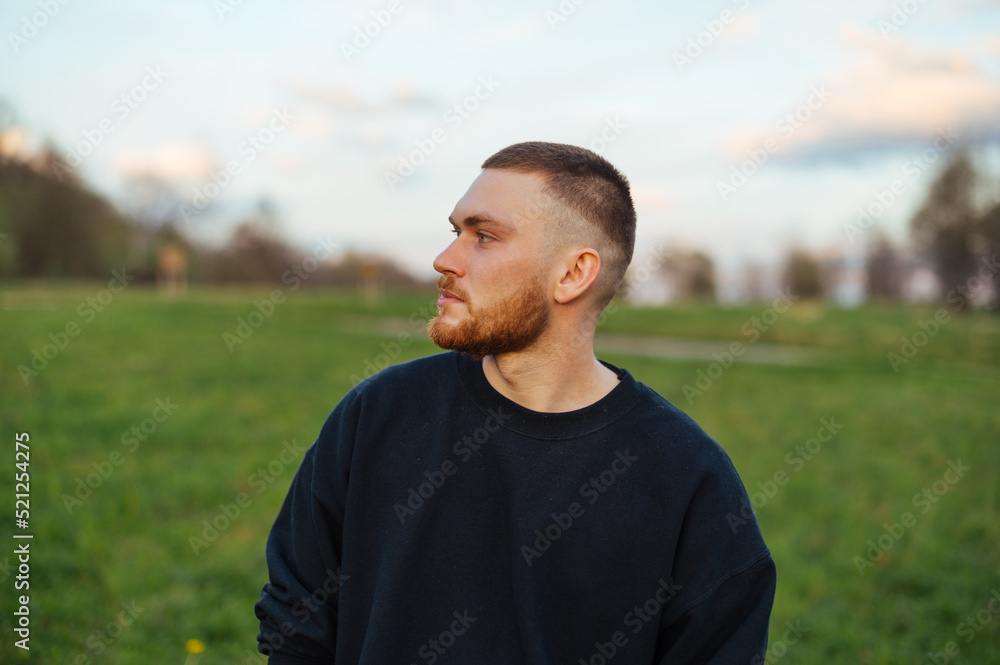 Portrait of a handsome young man with a beard in casual clothes standing in a field in nature and looking away with a serious face. Portrait of a handsome young man with a beard in casual clothes standing in a field in nature and looking away with a serious face.