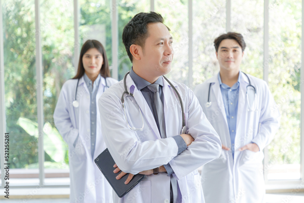Portrait of asian senior doctor standing in medical office while using tablet.Young Male and Female doctor in lobby of hospital on background. Portrait of asian senior doctor standing in medical office while using tablet.Young Male and Female doctor in lobby of hospital on background.