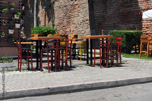Empty tables and chairs in Albanian sidewalk cafè.  Flower arrangements in buckets on the wall. Brick wall in the background. © RandiGrace
