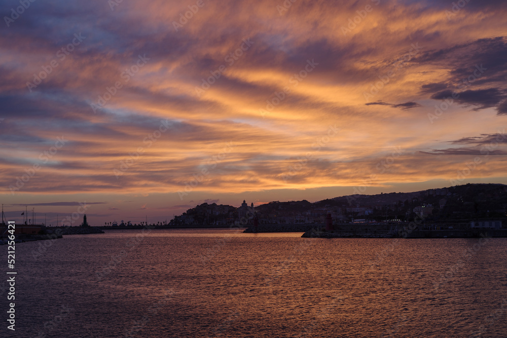 Dramatic colorful clouds at sunset with cityscape silhouette, Imperia, Liguria, Italy