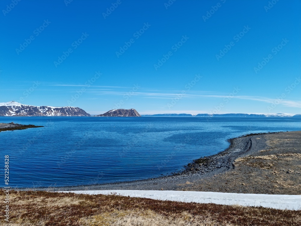 blue sea and snowy sea shore in Finnmark with massive mountains in the far background