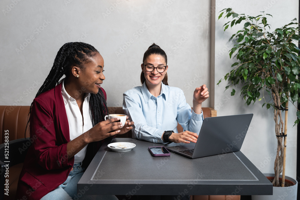 Two successful business freelance woman working in cafeteria on laptop. Wireless e commerce business meeting by two confident females in the coffee shop on computer. Two successful business freelance woman working in cafeteria on laptop. Wireless e commerce business meeting by two confident females in the coffee shop on computer.