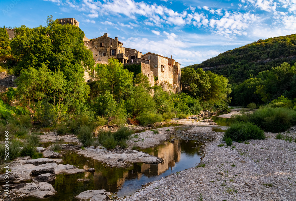 Montclus in C`eze valley near Avignon and Ardèche canyon is a popular and beautiful ancient village with castle. Scenery seen from river bridge with low water on a hot summer evening before sunset.
