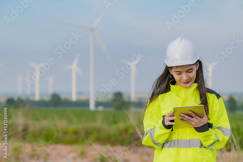 women engineer working and holding the report at wind turbine farm Power Generator Station on mountain,Thailand people