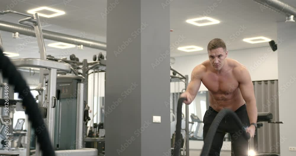 Athletic guy focused on fitness workout with ropes in the gym Athletic guy focused on fitness workout with ropes in the gym