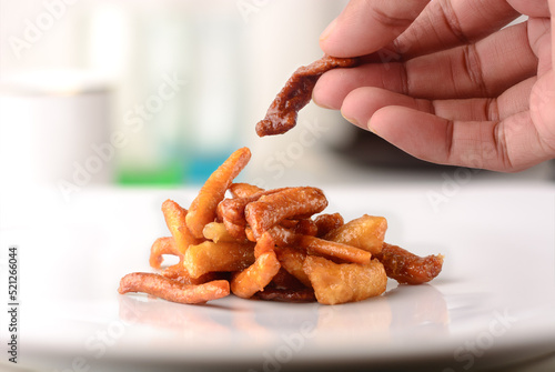 hand taking a piece of savory and crunchy snack coated with sugar syrup, traditional and popular indian sweet murukku on a white plate, soft-focus background photo