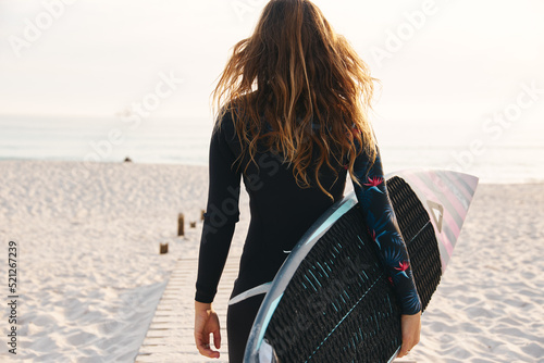 Female Extreme Sports Adventurer At The Beach Walking Down Jetty With Surf Board Or Kite Surfing Wearing Wetsuit