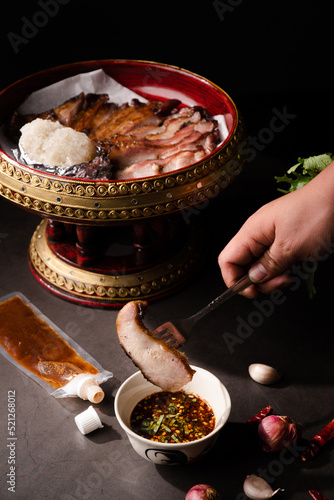 Close up fork pick up and dip a piece of grill pork jowl in spicy sauce thai food with sticky rice