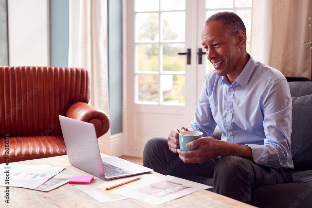 Mature Male Architect Or Interior Designer Working From Home Looking At Designs On Laptop Mature Male Architect Or Interior Designer Working From Home Looking At Designs On Laptop