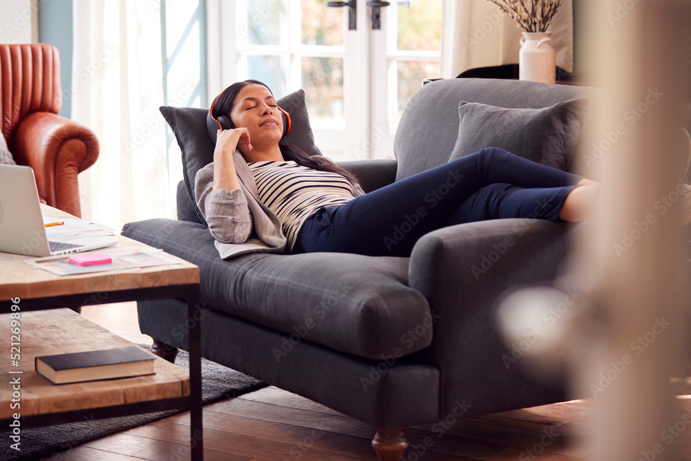 Woman Working From Home Taking A Break Lying On Sofa Listening To Music On Wireless Headphones Woman Working From Home Taking A Break Lying On Sofa Listening To Music On Wireless Headphones