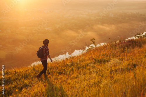 Anonymous man walking on meadow and admiring mountainous valley at sunrise