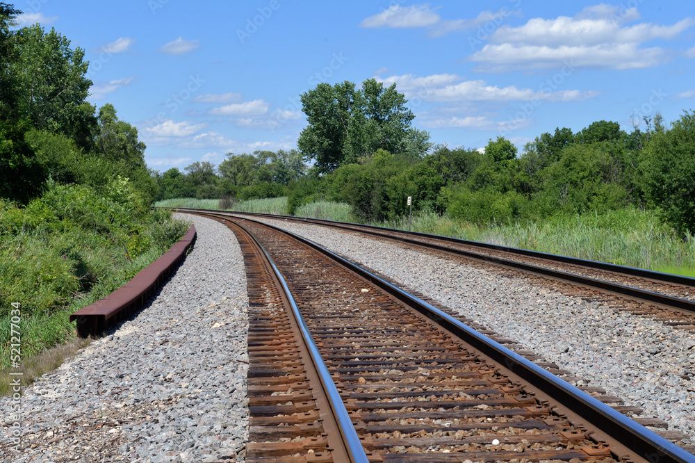 A pair of vacant railroad track bend around a curve in rural northeastern Illinois. The tracks are a main line tangent along with a passing siding on the railway.