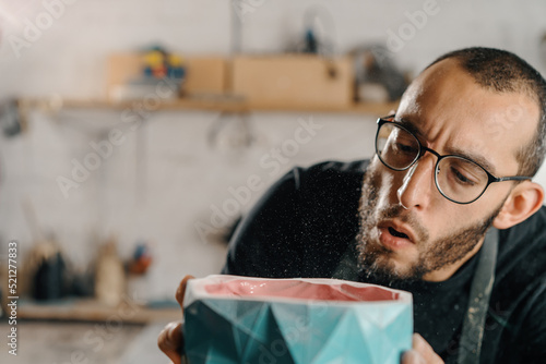 Close-up: a male artist sculptor artisan blows dust off an item. Handmade workshop.