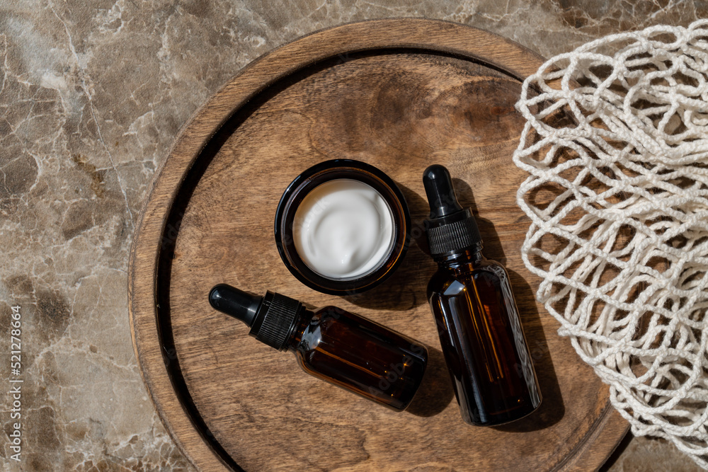 anti-aging collagen facial serum in dark glass bottle and face cream on wooden tray on brown background with copy space. Natural Organic Cosmetic Beauty Concept. Mockup for branding