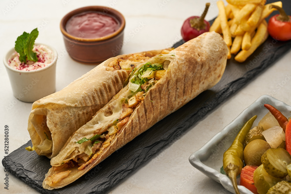 Shawarma Sarooh with fries, pickle, ketchup and dip served in a dish isolated on grey background side view of fastfood Shawarma Sarooh with fries, pickle, ketchup and dip served in a dish isolated on grey background side view of fastfood