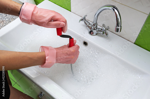 Woman in protective rubber gloves unblocking  a clogged sink with a probe or drained cable at home.  photo