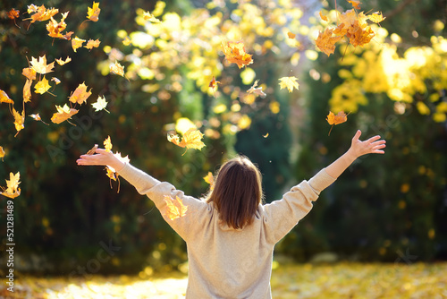 Young woman is having fun while walking through the forest on a sunny autumn day. Girl plays with maple leaves and throws them up. Rustle of leaves.