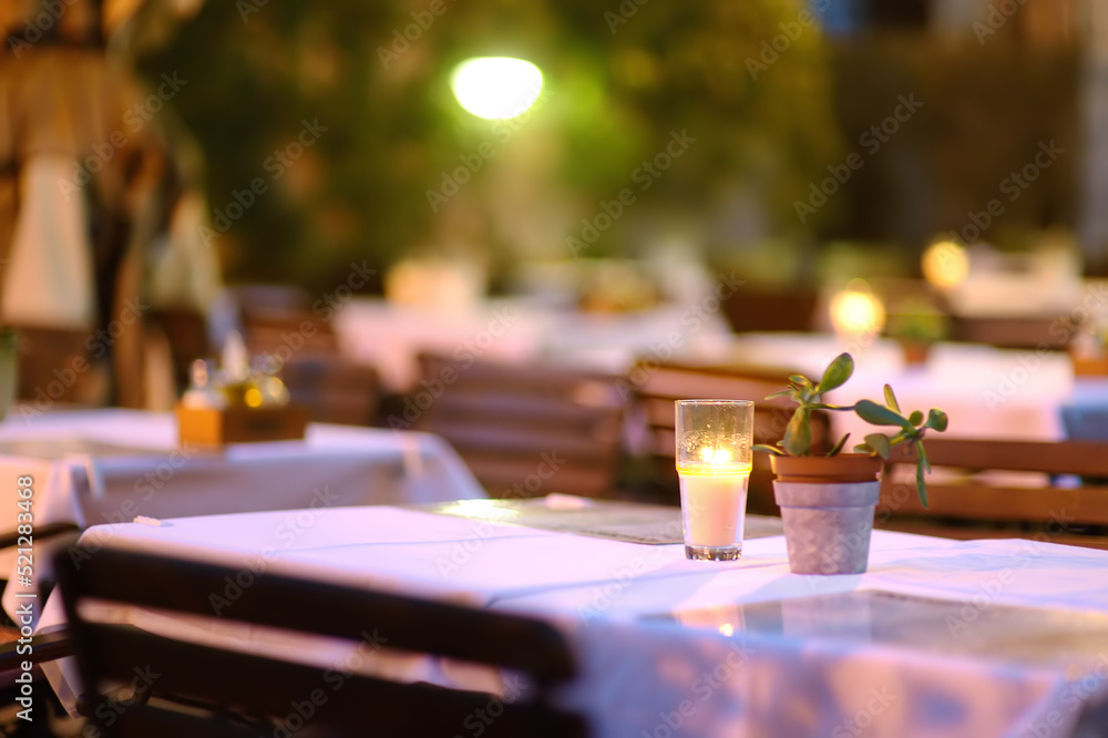 Empty outdoor cafe at dusk. Stylish table decoration with borning candle and natural plant.