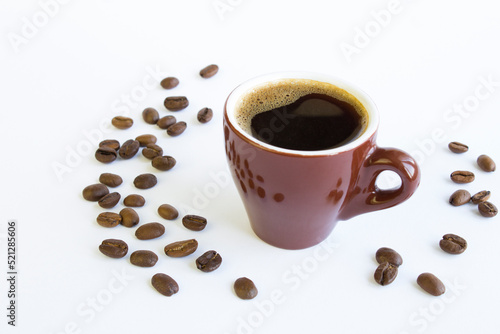 Black coffee in the brown cup and coffee beans on the white background. Closeup.