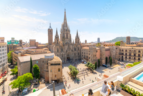 Young couples enjoy drinks with a view of the gothic Barcelona, Spain cathedral from a rooftop terrace with cafe and swimming pool over the Placita de la Seu plaza on a sunny summer day. photo