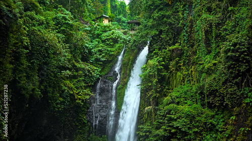 waterfall with rocks among tropical jungle with green plants and trees and water falling down