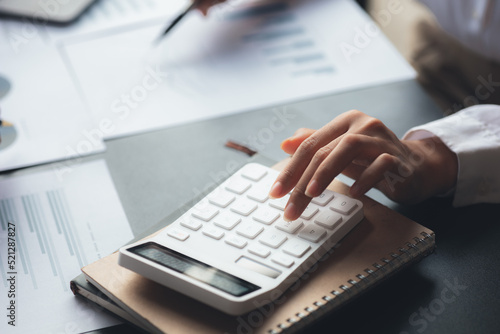 A businessman is using a white calculator to calculate financial numbers, he is sitting in his private office, the businessman examines the financial data from the corporate finance chart.