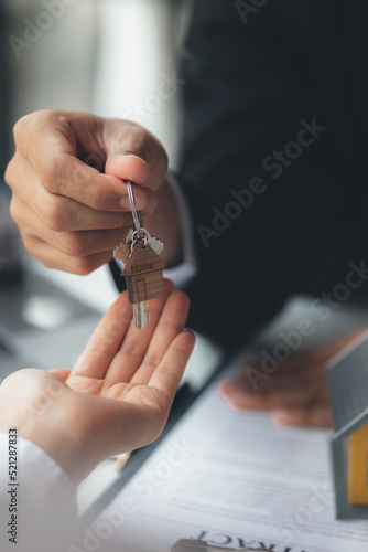 A home rental company employee is handing the house keys to a customer who has agreed to sign a rental contract, explaining the details and terms of the rental. Home and real estate rental ideas.