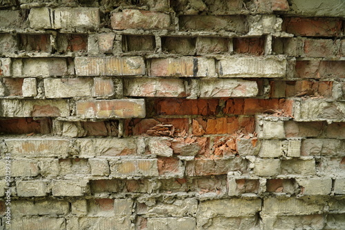 An old crumbling wall with destroyed bricks between a strong masonry mortar.