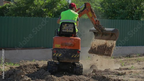 A man on a mini-excavator levels a piece of land, loosens the soil