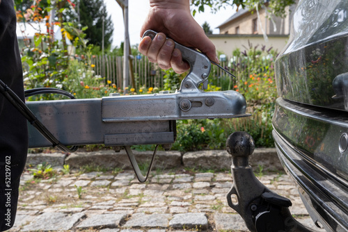 man's hand checks the fixation of the trailer closed hitch lock handle on the towing ball towbar of the car closeup, the safety of driving with a trailer on the road photo