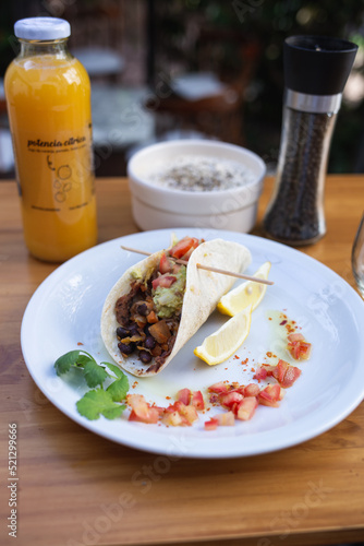 taco dish with vegetables and sauces, orange juice and sauce on the table