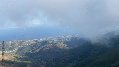 Scenic view of green mountains against a blue sea on a foggy day in Messina, Italy photo