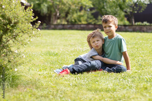 Two little brother boys lie on the grass and hug. Family ties and friendship concept © Marina