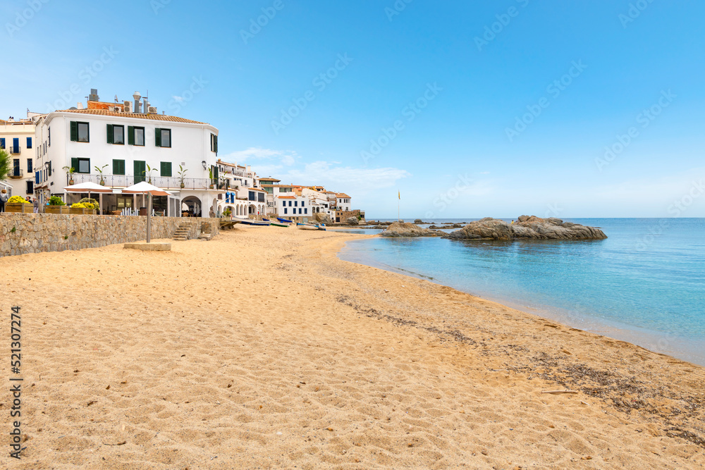 The sandy beach and turquoise Mediterranean Sea along the Costa Brava coast at the whitewashed fishing resort town of Calella de Palafrugell, Spain.