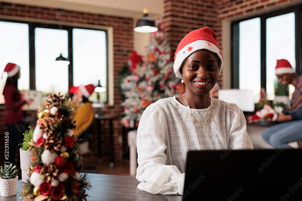 Portrait of african american woman with santa hat working on business at  company office filled with christmas decorations and tree lights. Using  laptop in startup workplace with xmas decor. Photos | Adobe