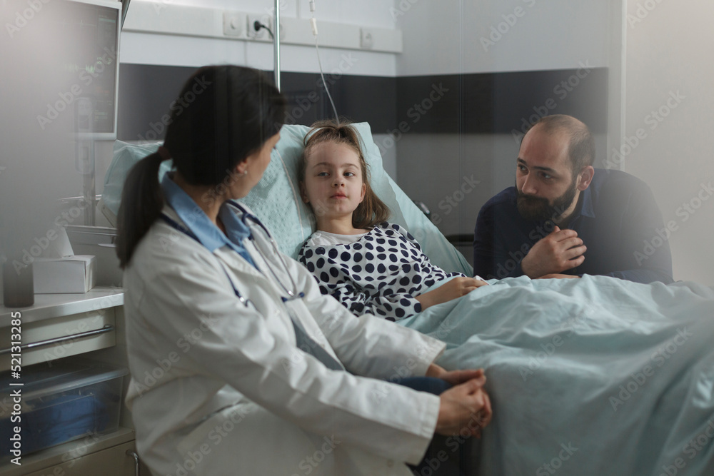 Pediatrician examining sick girl disease symptoms while resting in patient bed. Doctor expert discussing with girl about her health condition while caring father sitting beside ill daughter. Pediatrician examining sick girl disease symptoms while resting in patient bed. Doctor expert discussing with girl about her health condition while caring father sitting beside ill daughter.