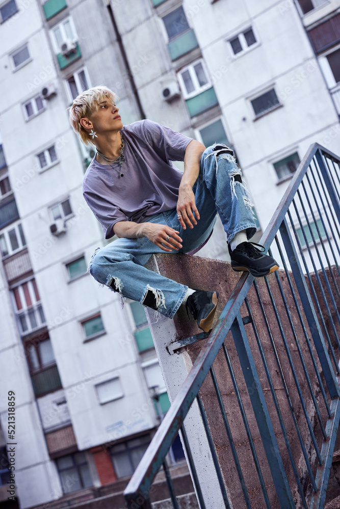 A teenage boy sits on the concrete wall in the urban exterior, looking away and feeling lonely.