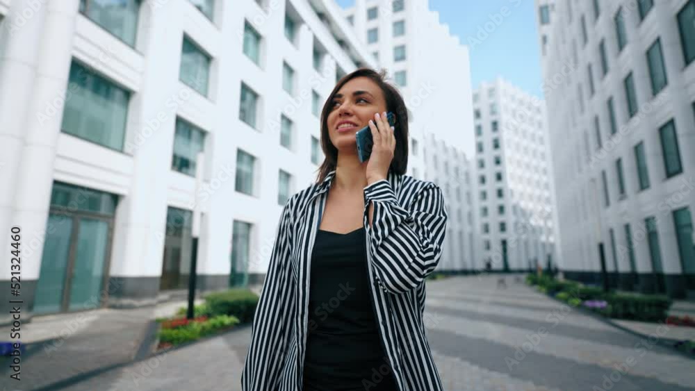 joyful woman is walking in modern city district and talking by cell phone, portrait in movement