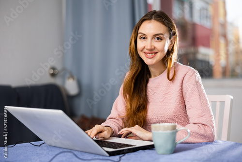 Portrait of a young woman working on a laptop, sitting at a table in an apartment