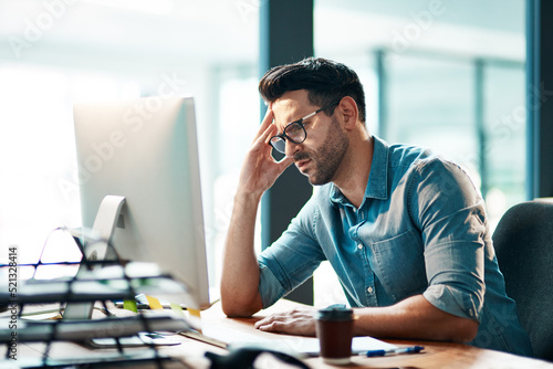 Stress, headache and frustrated business man working on computer in an office, annoyed and anxious. Male under pressure from a workload and deadline. Depressed guy experiencing burnout at work