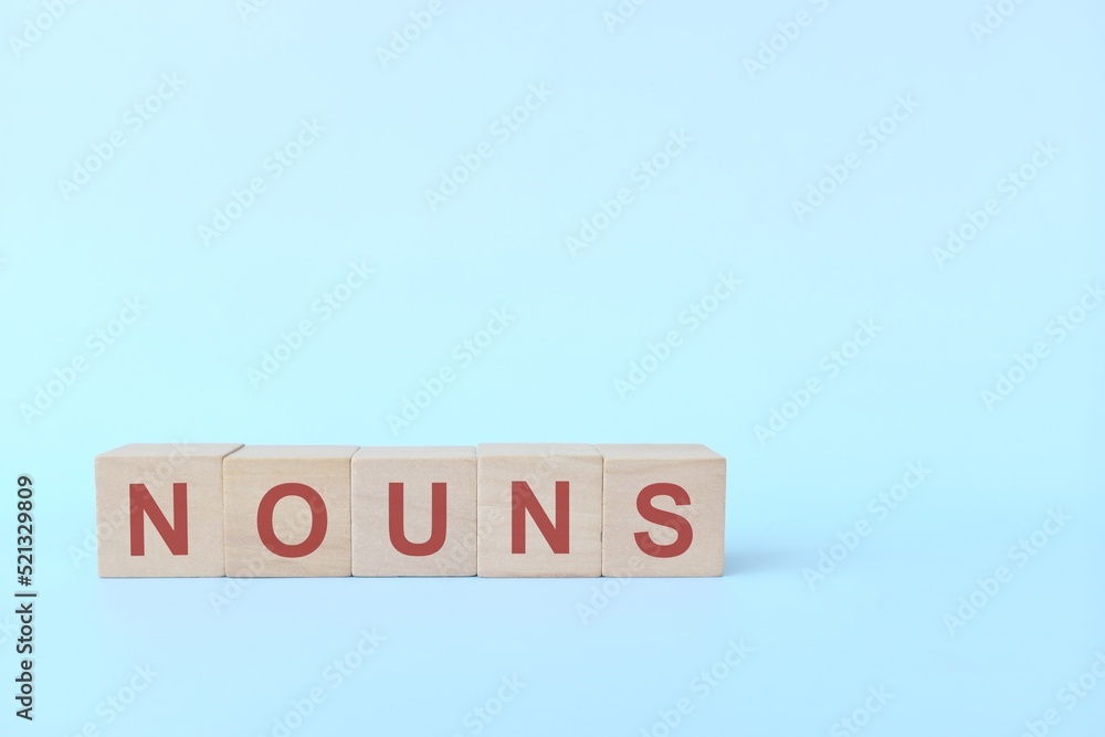 Nouns concept in English grammar education. Wooden block crossword puzzle flat lay in blue background. Nouns concept in English grammar education. Wooden block crossword puzzle flat lay in blue background.