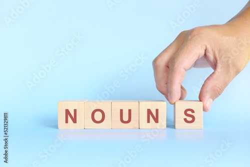 Nouns concept in English grammar education. Wooden block crossword puzzle flat lay in blue background. 