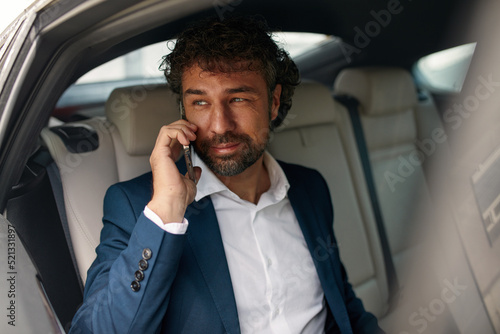 Businessman is Commuting from Office in a Backseat of Her Luxury Car. Male Entrepreneur Using Smartphone while in Transfer Taxi in Urban City Street