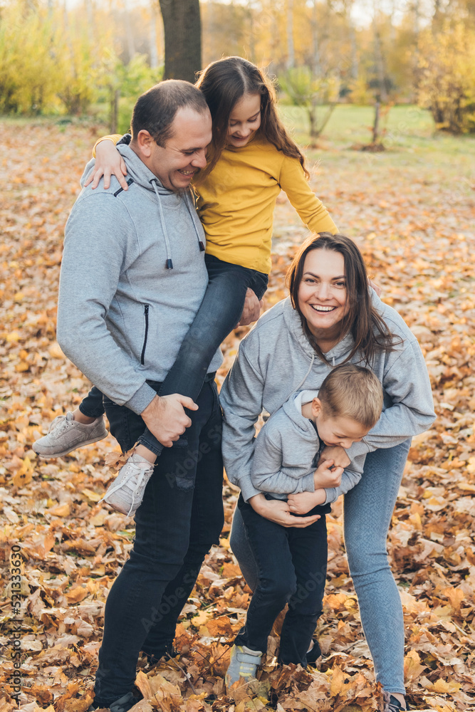 Fototapeta premium Happy mother, father and two little kids posing in the autumn park. Concept of family spending time together on vacation. Childhood, parenting, relax concept